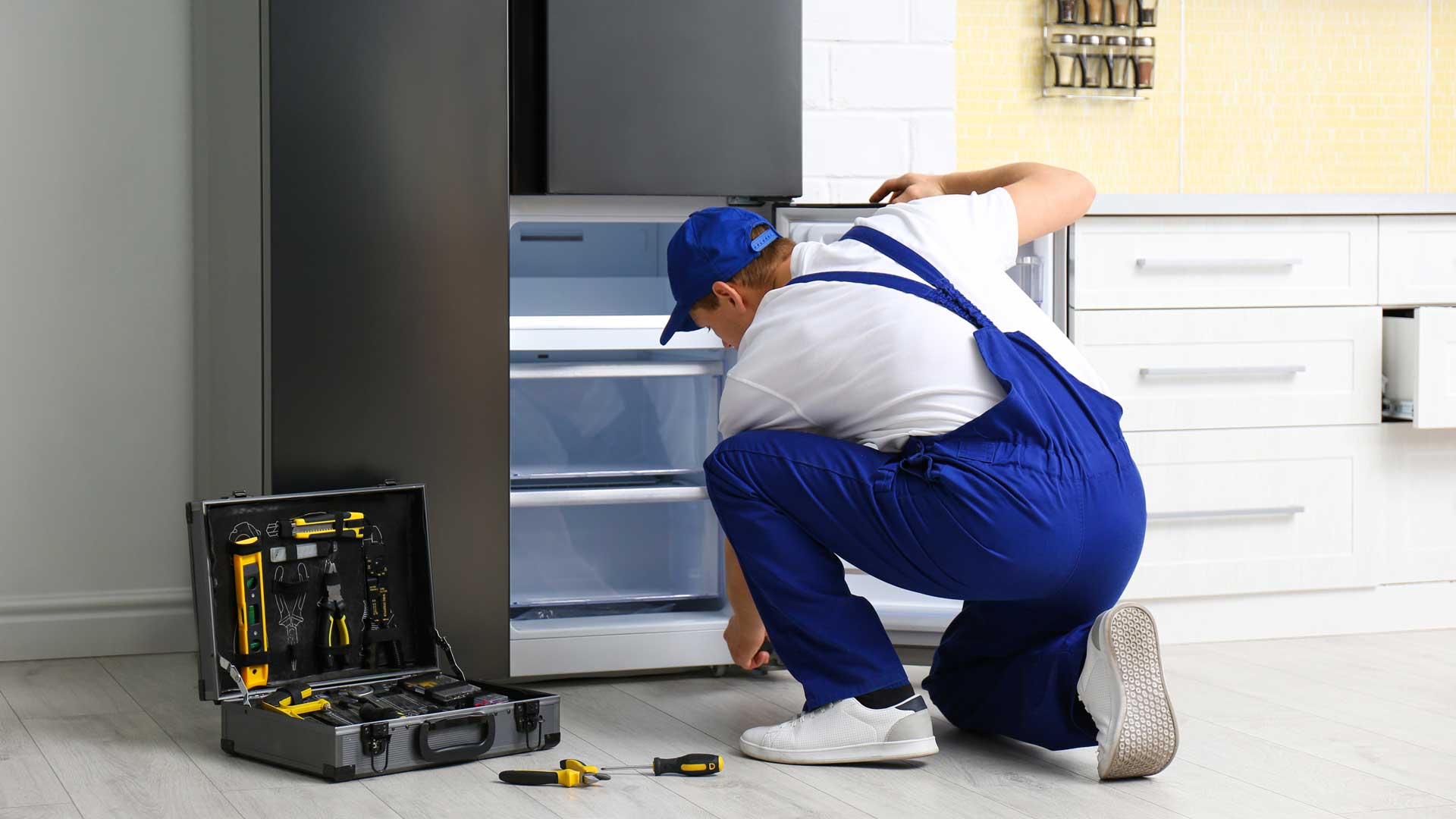 Man in blue uniform repairing the freezer drawer of a refrigerator
